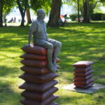 Bildende Kunst: Skulptur einer sitzenden Figur auf Kissenstapel im Park. Kunst im öffentlichen Raum.