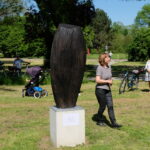 Bildende Künste: Holzskulptur im Park. Frau betrachtet Kunstwerk. Natur und Kultur vereint.