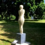 Bildende Kunst: Skulptur einer Frau im Park. Kunstwerk aus hellem Stein auf Sockel.