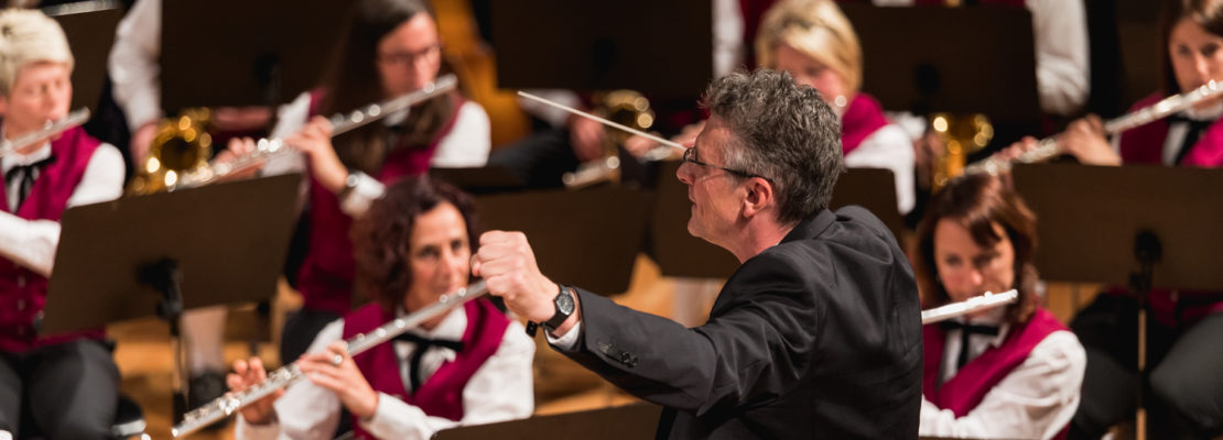 Orchesterdirigent leitet Musiker. Musikstadt mit Flöten und Blechbläsern.
