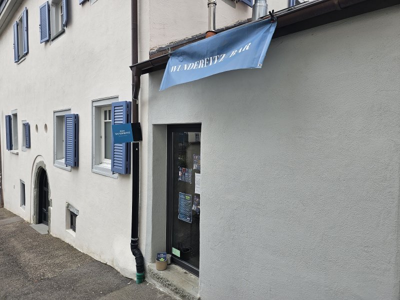 Fassade mit Fensterläden, Wunderfitz Bar Schild. Eingangstür und Gasse. Architektur in Stein am Hang.