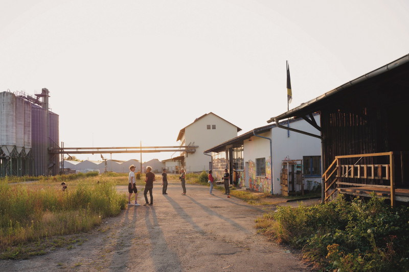Gruppe von Personen vor Industrielandschaft mit Getreidesilos bei Sonnenuntergang. Ländliche Szene, Gebäude und Menschen.