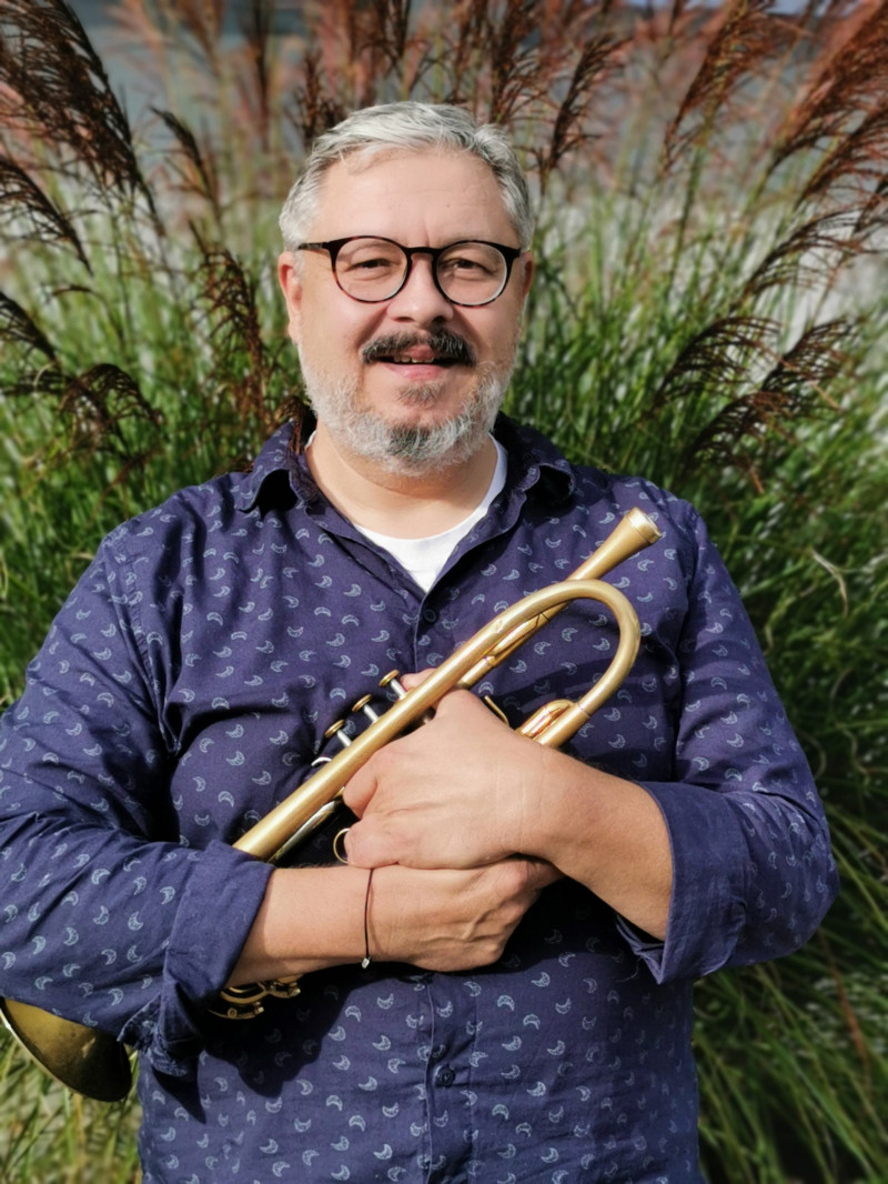 Mann mit Trompete vor Ziergras. Musiker mit Brille und Bart hält Musikinstrument.